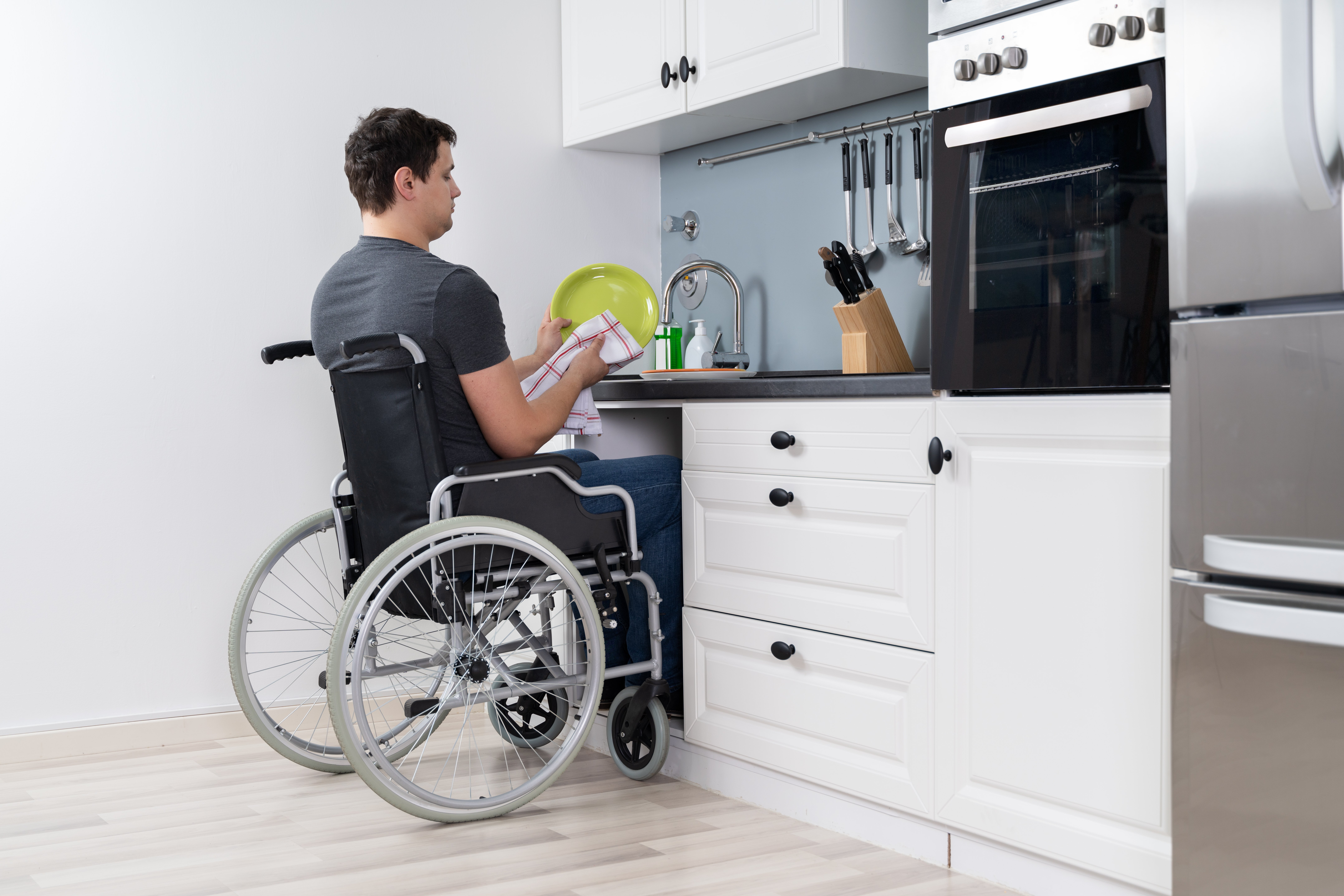 Hombre discapacitado sentado en cocina en sillones lavando y limpiando platos